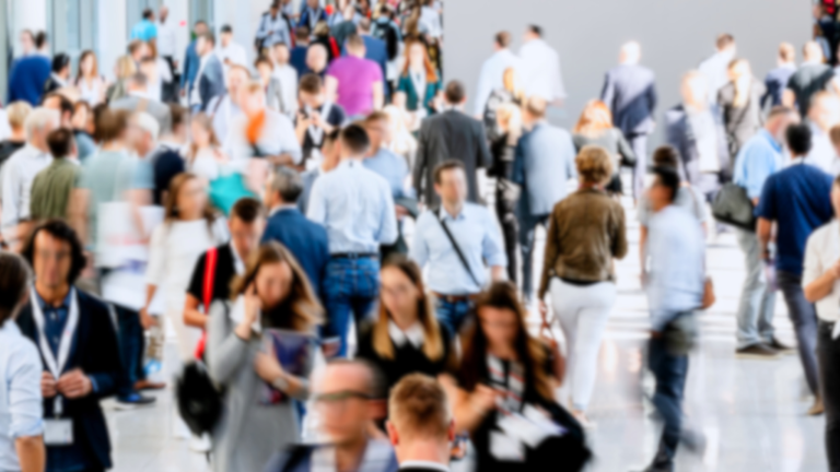 A large crowd of people walking in a convention center, some carrying bags and wearing badges, with a variety of attire including casual and business clothing, highlighting the gathering's purpose of creating a responsive talent pool for actionable hiring.